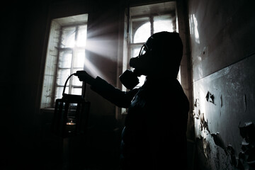 Fototapeta na wymiar Spooky person with gas mask holding a lamp in dense fog in an abandoned building with eerie feeling. 