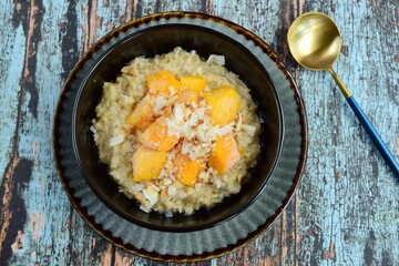Oat porridge breakfast with cubed mango and coconut chips