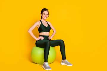 Obraz premium Sportive lady sit big green fit ball arms by sides wear suit top pants sneakers isolated yellow color background