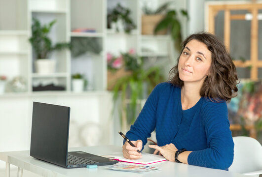 A young brunette woman uses a laptop in her office or at home.