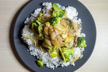 Beef and broccoli on top of rice on a plate.