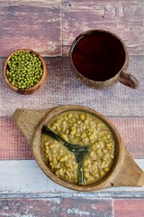 Bubur Kacang Hijau, Indonesian dessert made from mung beans cooked in coconut milk and palm sugar flavored with pandan leaves. Served on wooden bowl with tea