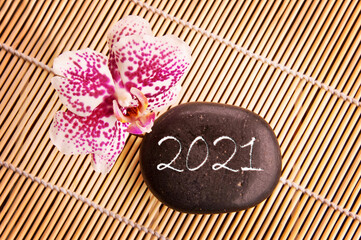 Obraz na płótnie Canvas 2021 written on a black pebble with pink orchid, zen new year greeting card