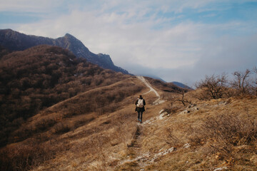 A man walks along a path up the mountain with a backpack against a blue sky in autumn.