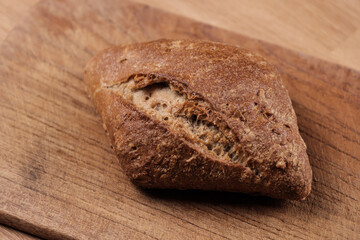 Ein frisches dunkles Brötchen auf einem hölzernen Brettchen