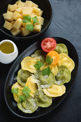 Black plate with ravioli and parmesan cheese, studio shot on a black stone background, elevated view