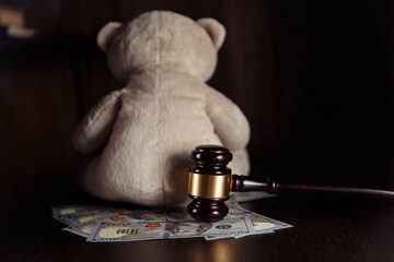 Alimony payment. Dollar banknotes, judge gavel and teddy bear on a wooden table close-up. Divorce, separation and alimony concept.