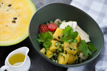 Yellow watermelon cubes, herbed cucumber and cheese salad served in a green bowl, studio shot, selective focus