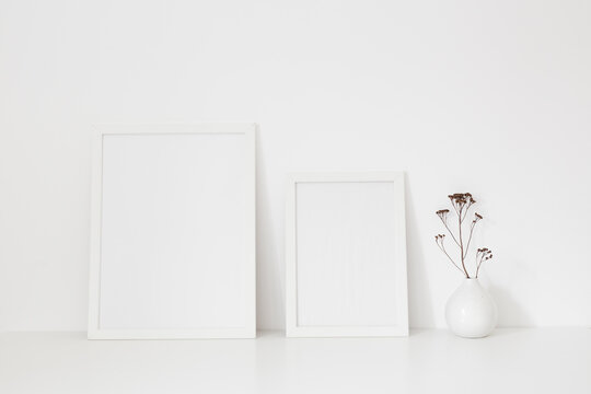 Mock up two white frames and dry twigs in vase on book shelf or desk. White colors..