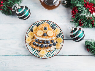 Christmas tree shaped sweet crepes filled with cream greek yogurt, banana and blueberries on white wooden table with winter holiday decor.