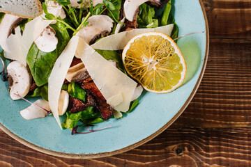 Salad with grilled meat, mushrooms and herbs on wooden background