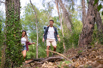 Happy couple traveling together and hiking in forest. Two Caucasian backpackers walking through woods, chatting, smiling and enjoying nature together. Tourism, adventure and summer vacation concept