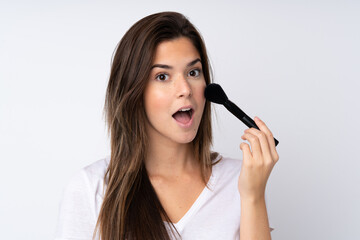 Teenager girl over isolated background holding makeup brush and surprised