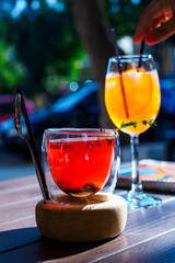 Siberian tea with cones, lingonberries and a sprig of thyme in a transparent glass with double walls against the background of aperol spritz on the cafe terrace