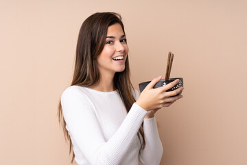 Teenager girl over isolated background holding a bowl of noodles with chopsticks