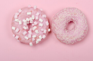 Two donuts with icing on pastel pink background. Copyspace