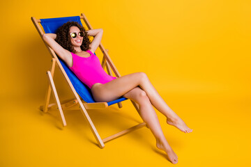 Photo portrait of woman lying in blue lounge chair relaxing hands behind head wearing eyeglasses pink bodysuit isolated on vivid yellow colored background