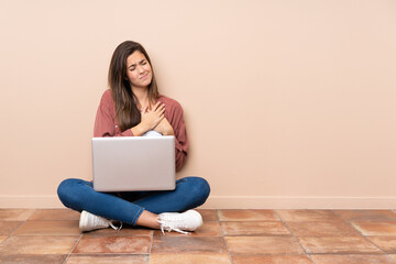 Teenager student girl sitting on the floor with a laptop having a pain in the heart
