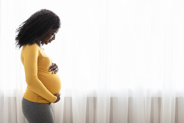 Beautiful pregnant black woman hugging her tummy at home - Powered by Adobe