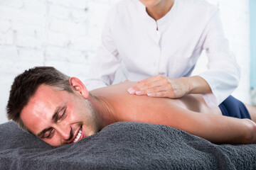Fototapeta na wymiar Portrait of young man enjoying relaxing massage by professional masseuse