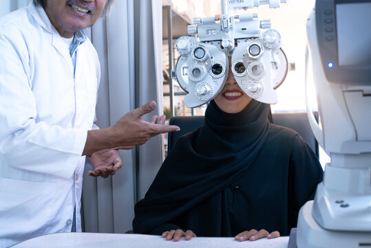 Muslim Optometrist Controls The Oculist Display, Muslim Woman Wear Black Hijab Looking Through Optical Phoropter During Eye Exam, Diagnostic Ophthalmology Equipment, Selective Focus