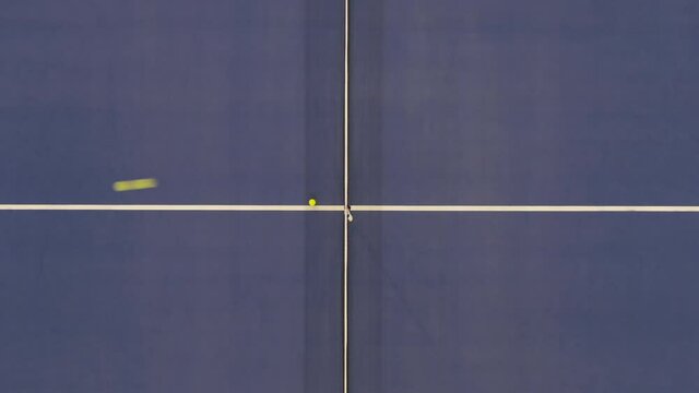 Top view of indoor court with yellow tennis ball flying from left to right and backwards. Unknown players training in competitive sports game in gym. Professional sport concept.