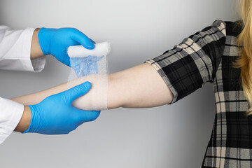 The traumatologist puts a bandage on the elbow of the female patient. The concept of help with fractures and sprains. The technique of applying a cruciform bandage.