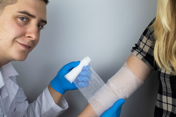 The traumatologist puts a bandage on the elbow of the female patient. The concept of help with fractures and sprains. The technique of applying a cruciform bandage.