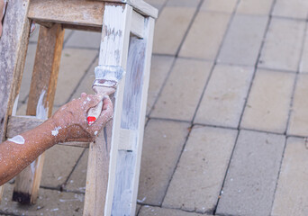 Senior man holding brush for paint white on old wooden chair without a backrest Hand of man. Old...
