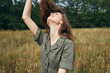 Woman in green jumpsuit holds her hair looking up fresh air