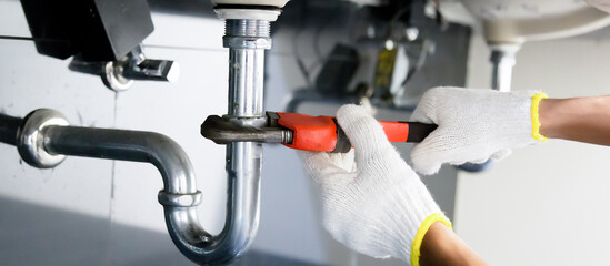 Plumber fixing white sink pipe with adjustable wrench.