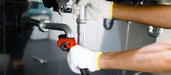 Plumber fixing white sink pipe with adjustable wrench.