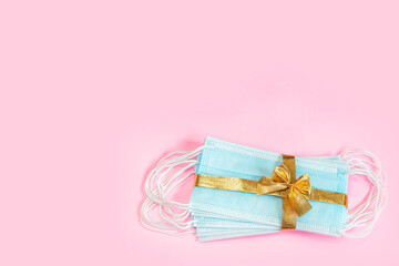 Medical protective masks with golden ribbon isolated on pink background. A gift for Christmas and New Year 2021. Coronavirus pandemic concept.