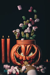 Halloween candy rain.
Artistic Halloween-themed still life in which "Halloween magic" is represented with a shower of candy falling into a pumpkin-shaped basket while a girl's hand tries to catch one 