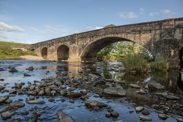 Fototapeta premium Large stone bridge crossing the river ribble near Clitheroe. Edisford bridge with rocks in the foreground 