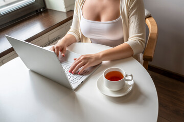 Lonely woman freelancer enjoying having breakfast with cup of coffee working on laptop sitting near window in cafe at morning. View on bust of female