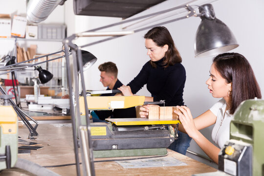 Young female architect working on fret saw, creating details for new architectural model in design bureau