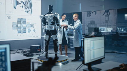 In Robotics Development Laboratory: Chief Female Engineer and Top Male Scientist Work on a Bionics Exoskeleton Prototype. Designing Powered Exosuit to Help Disabled People, Hard Labor Workers