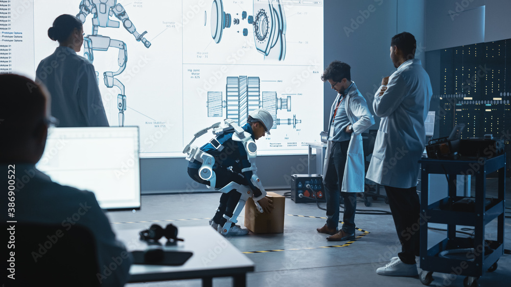 Leinwandbilder In Development Laboratory: Engineers Look at Robotics Exoskeleton Prototype Presentation with Person Testing it, Lifting Heavy Carboard Box. Designing Wearable Exosuit to Help Warehouse Workers