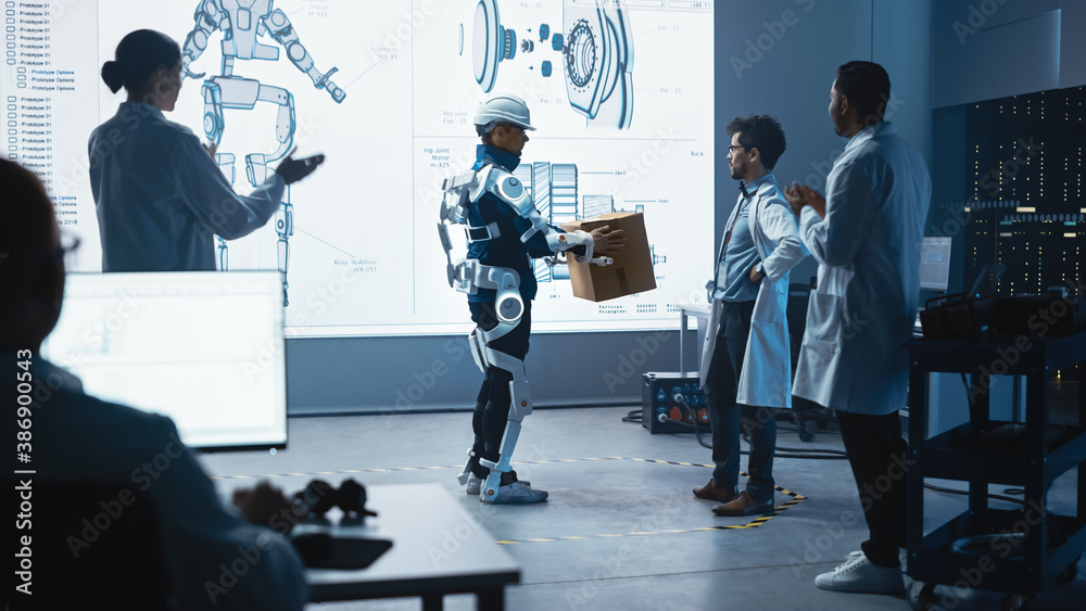 Leinwandbilder In Development Laboratory: Engineers Look at Robotics Exoskeleton Prototype Presentation with Person Testing it, Holding Heavy Carboard Box. Designing Wearable Exosuit to Help Warehouse Workers