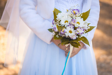 bride's hands with flowers on a background of autumn foliage. Bride with a bouquet