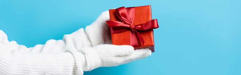 panoramic crop of woman in gloves holding gift box on blue