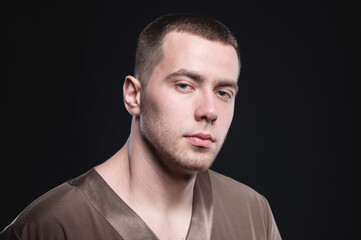 Studio portrait in low key manly attractive male physiotherapist massage therapist in contrast light in overalls on a black background