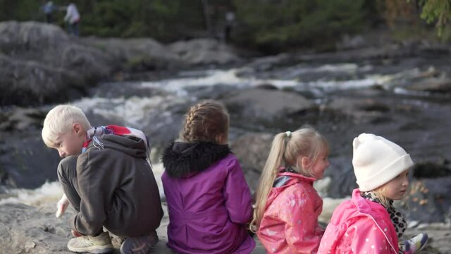 Children sit on a rock and look at a mountain river during a family hike in the Republic of Karelia, Russia.