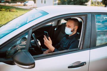 Portrait of a businessman with a protective mask holding a phone in his hand while sitting in a car. Business conversation on the way to work during the pandemic COVID - 19 coronavirus