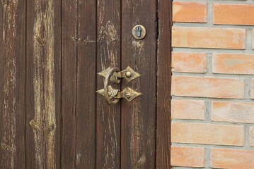 old metal doorknob on a wooden brown door near a brick wall in the street