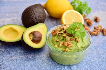 Avocado sauce with walnut and parsley in glass jar. Blue background
