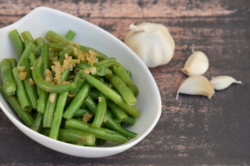 Sautéed green beans with garlic in a bowl on wooden background