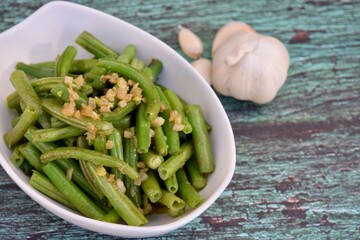 Sautéed green beans with garlic in a bowl on wooden background