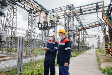 Engineers electrical substations conduct a survey of modern high-voltage equipment in the mask at the time of pandemia. Energy. Industry